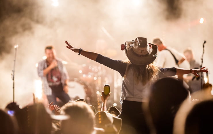 A woman in a cowboy hat sitting on somebody's shoulders as she watches a concert.