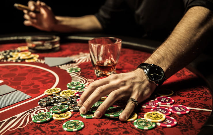 A man playing poker while drinking whiskey and smoking a cigar.